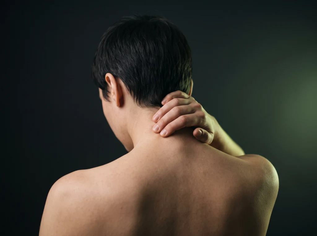 Person rubbing their neck with one hand, dark background